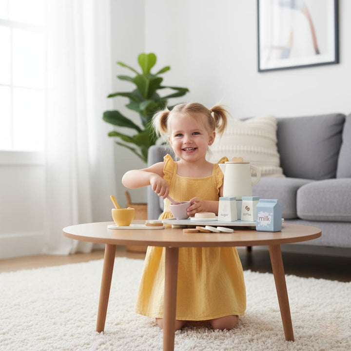 Child in a yellow dress playing with toy kitchen items on a wooden table in a living room.