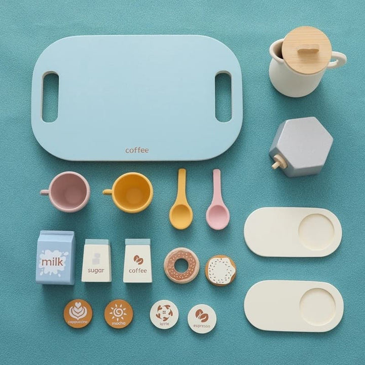 Set of toy coffee-making items including a cutting board, cups, spoons, and donuts on a teal background.